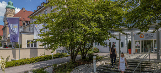 Entrance area of the Schoen Clinic Munich Harlaching with trees and visitors in summer