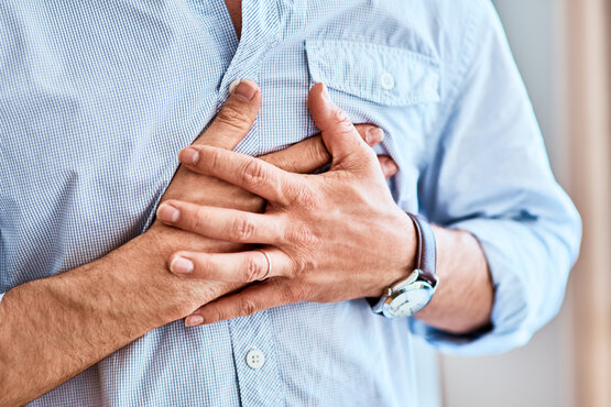 Man in light blue shirt holding his chest with both hands, symbolic image for heart attack or acute heart problems