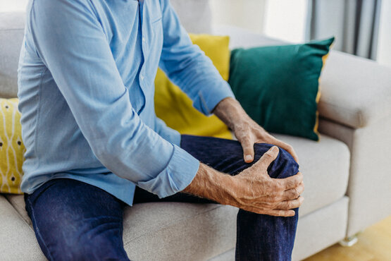 Man sitting on the sofa holding his right knee due to knee pain