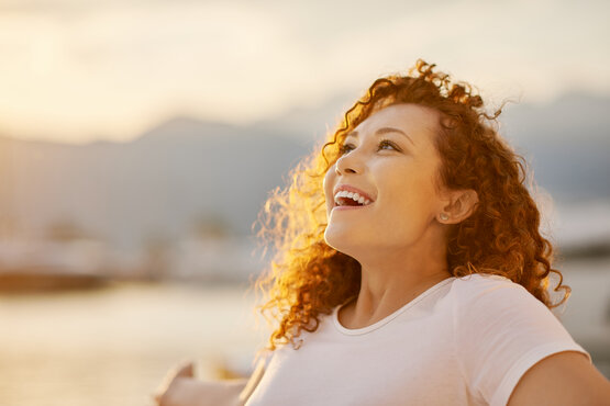 Smiling young woman with curly red hair relaxes and enjoys the sunset by the water.