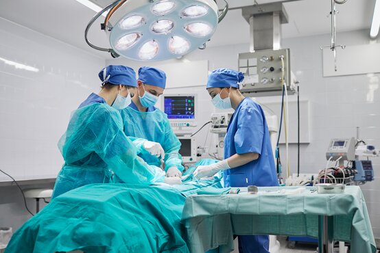 Three surgeons in sterile surgical clothing operate intently on a patient in a modern operating room