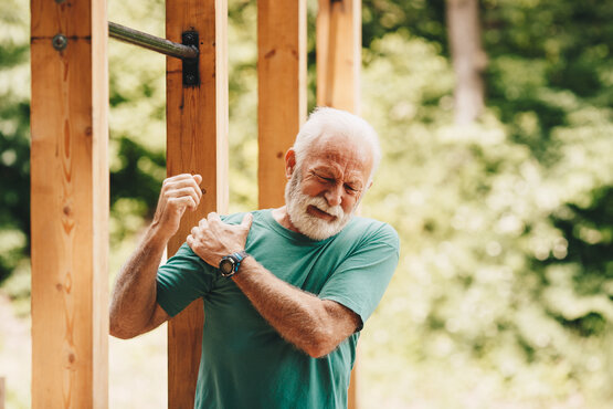 Elderly man holding his right shoulder in pain outdoors