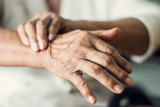Older hands, one gently checking the other's wrist against a neutral background