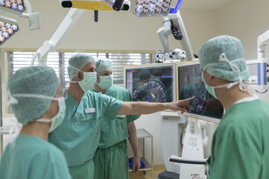 Surgical team in surgical attire jointly reviewing brain images on a large monitor in the operating theatre