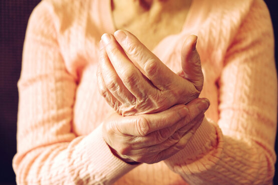 Close-up of elderly person in peach sweater massaging their left hand with right hand, showing signs of pain