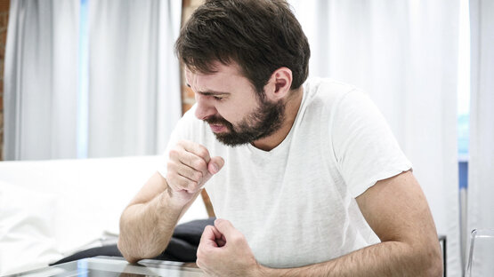 Man in white T-shirt coughs into his fist