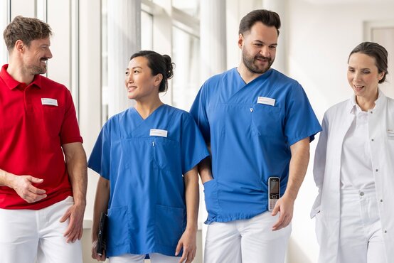Pflegekräfte und medizinisches Fachpersonal stehen lächelnd im hellen Klinikflur mit Tageslicht und moderner Ausstattung