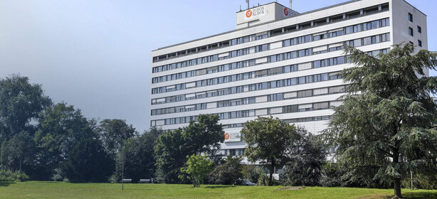 Multi-level, modern white clinic building of the Schön Klinik Düsseldorf, surrounded by green spaces and trees