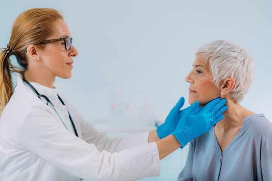 Female doctor palpates elderly woman's neck for thyroid or lymph node examination in clinic